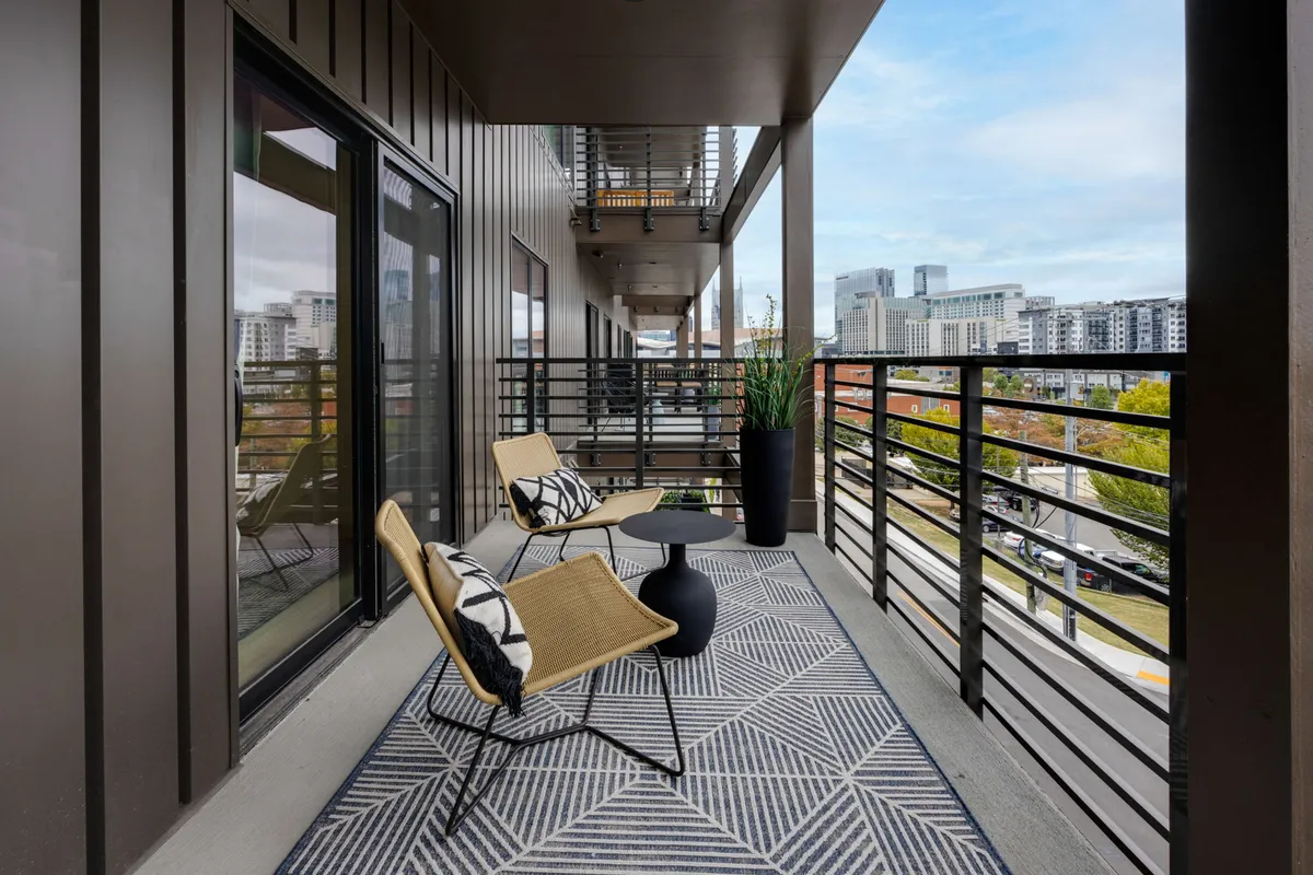 A contemporary private balcony setup with stylish chairs and a small table, offering an elevated view over the city. Lush planters add a touch of greenery, and the vantage point suggests a spot perfect for taking in skyline views, relaxing, or snapping photos before heading out for the night.