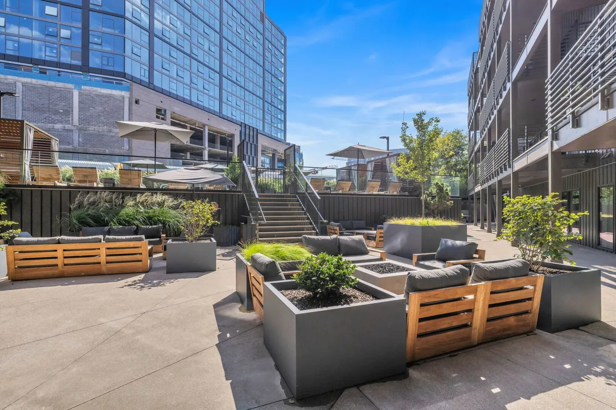 A contemporary outdoor lounge area with modern seating and lush greenery, perfect for relaxing or gathering with friends. Stairs lead to other levels, suggesting vibrant community life and multiple amenities.
