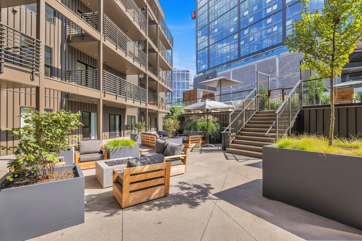 A contemporary outdoor lounge with modern furniture, lush green plants, and umbrellas inviting groups to relax, dine alfresco, or enjoy sunset views. The setting exudes comfort and sociability, perfect for BBQs or evening drinks with city views.