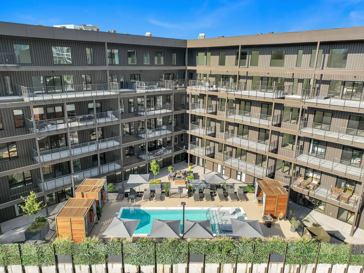 A vibrant exterior scene featuring a sparkling swimming pool surrounded by lounge chairs and lush landscaping, with balconies overlooking the area. The setting exudes a lively and social atmosphere, perfect for poolside gatherings and relaxation.