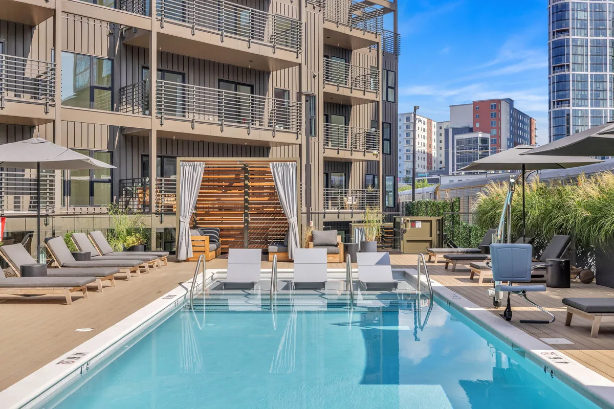 This exterior image showcases the sparkling swimming pool surrounded by lounge chairs, outdoor umbrellas, and the building facade. The pool area is lively yet relaxed, with plenty of space for socializing, sunbathing, and enjoying sunny weather.