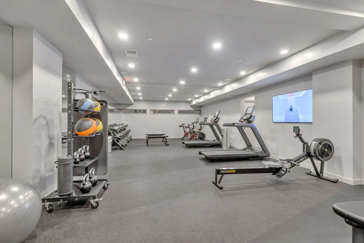 A well-equipped, energetic fitness center with treadmills, stationary bikes, rowing machines, and free weights. The space is modern and designed for individual or small-group workouts.