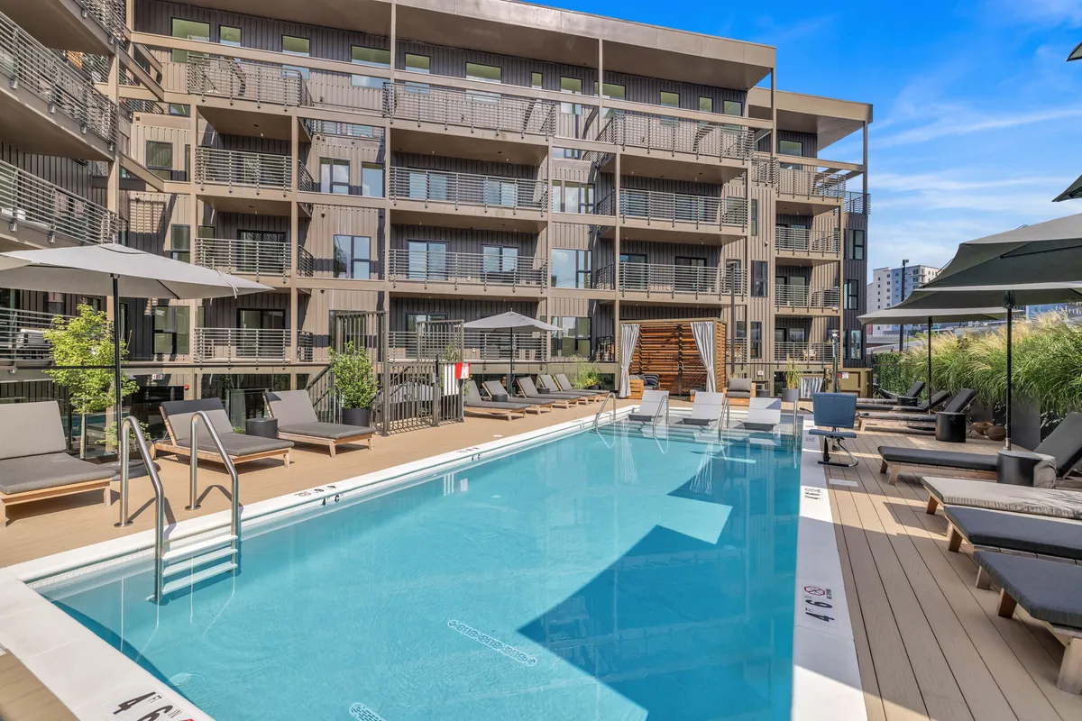 A bright outdoor swimming pool surrounded by lounge chairs, greenery, and the building’s façade. The space feels inviting, perfect for family relaxation and fun after a day of city adventures.