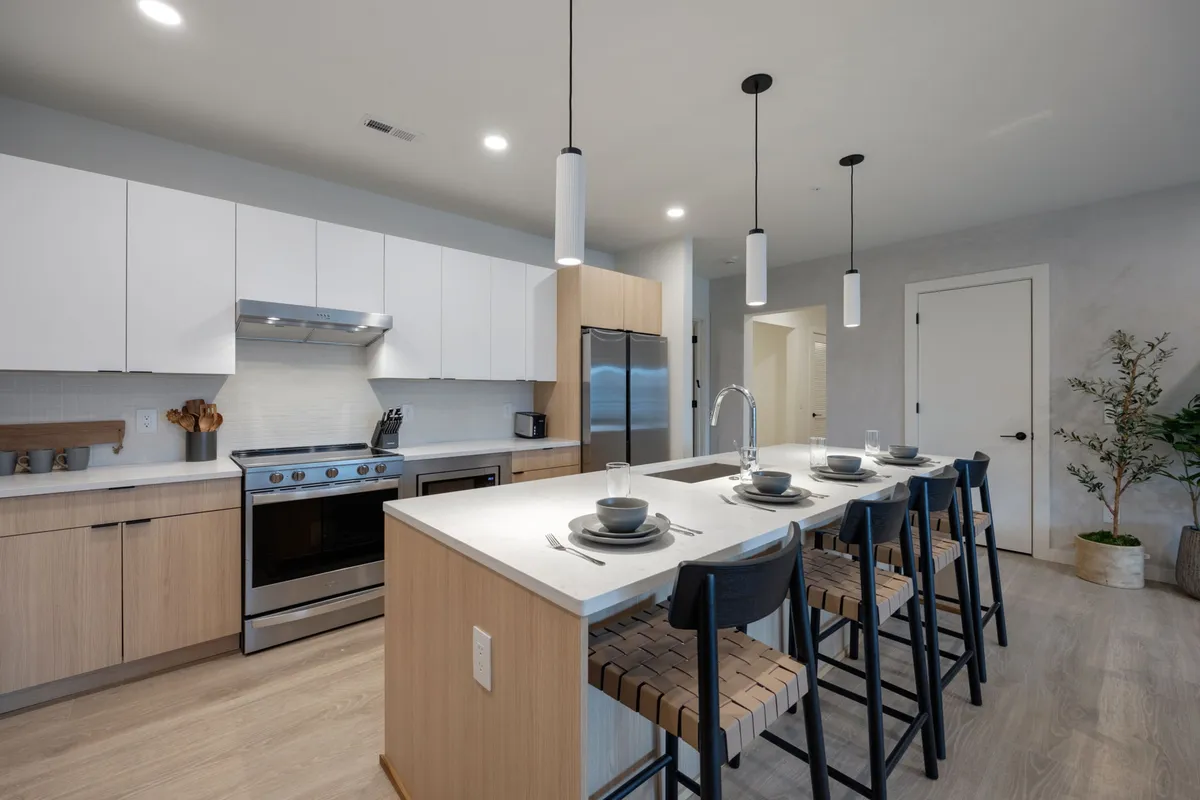 A contemporary kitchen with a large island, pendant lighting, stainless steel appliances, wooden cabinetry, and bar stools. The open layout encourages interaction and makes the space perfect for entertaining or casual meals.