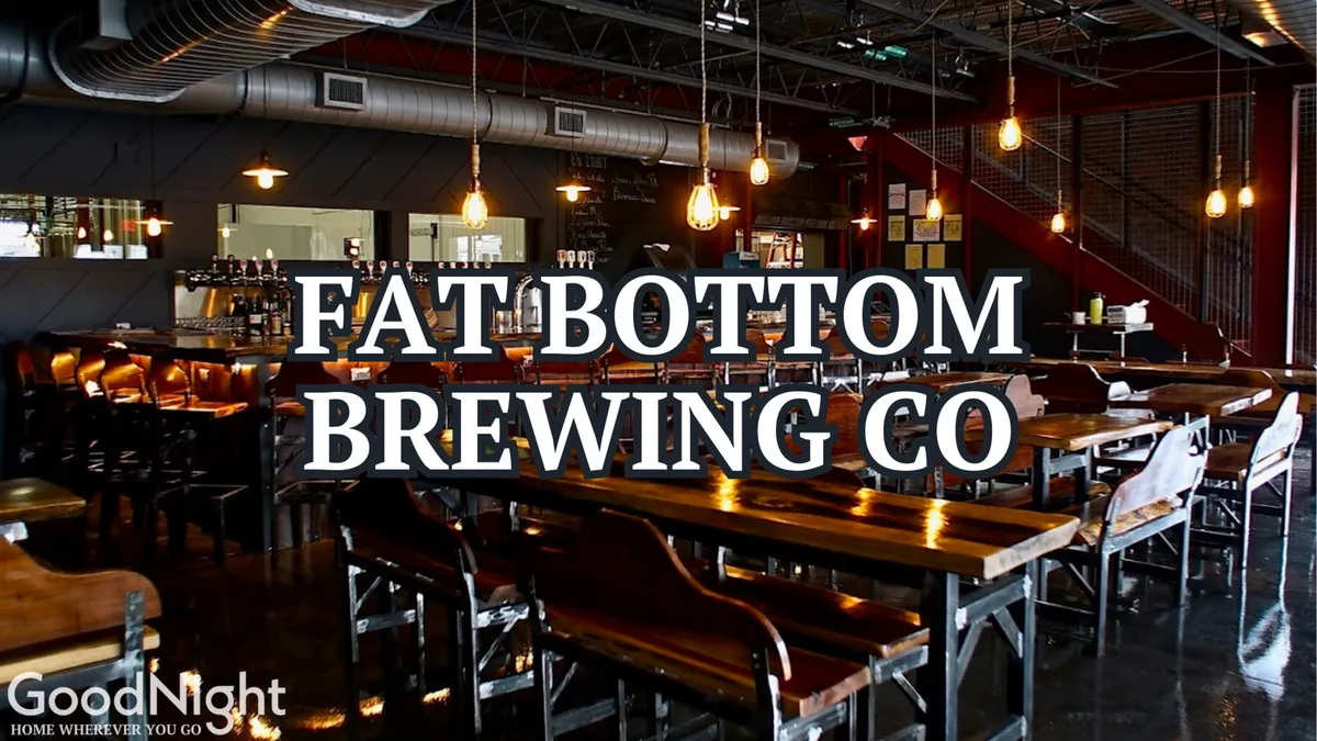 A lively interior of a brewery or communal dining space featuring long wooden tables, stylish pendant lighting, and a bustling bar area. Groups of people can be imagined socializing, sharing drinks, and enjoying the convivial atmosphere.