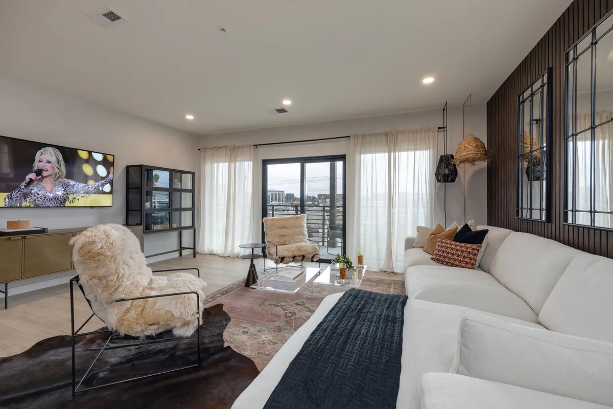 A spacious and stylish living room with a large sofa, decorative rugs, a television, and a window offering a glimpse of the view outside. The design is contemporary yet comfortable, inviting groups to gather for entertainment or relaxation.